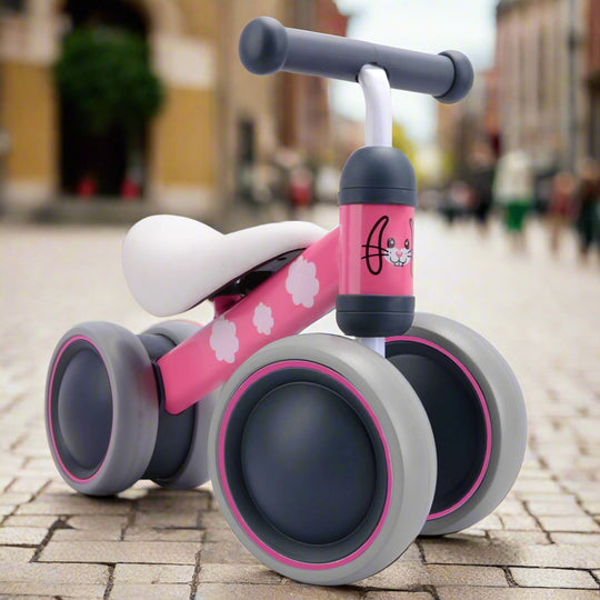 Pink and grey balance bike with rabbit design on a cobbled pavement background