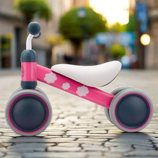 Pink balance bike with white seat and flower patterns on a cobbled pavement background