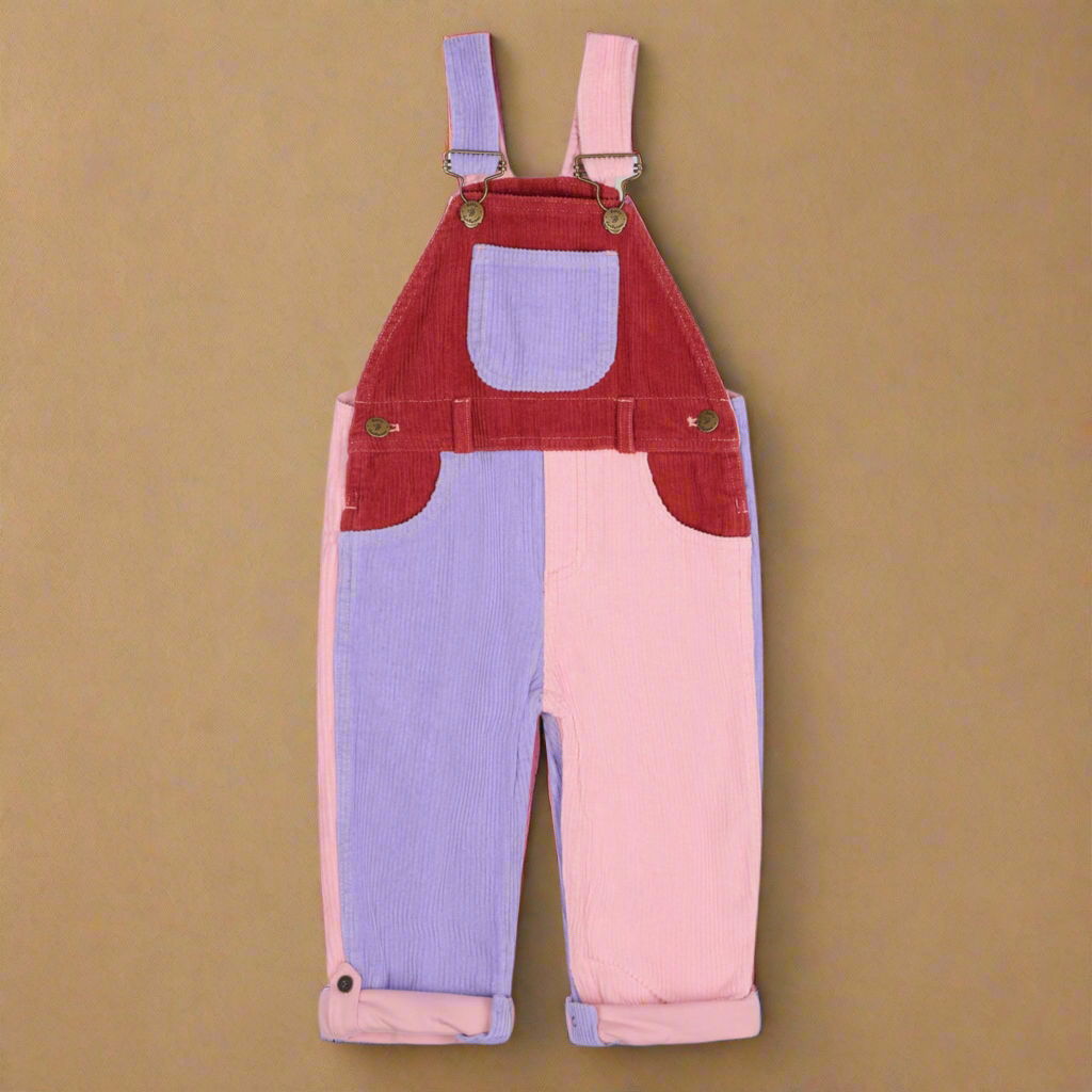Patchwork corduroy dungarees with blocks of red, pale lilac and pale pink with two side pockets and a central chest pocket, with brass buttons