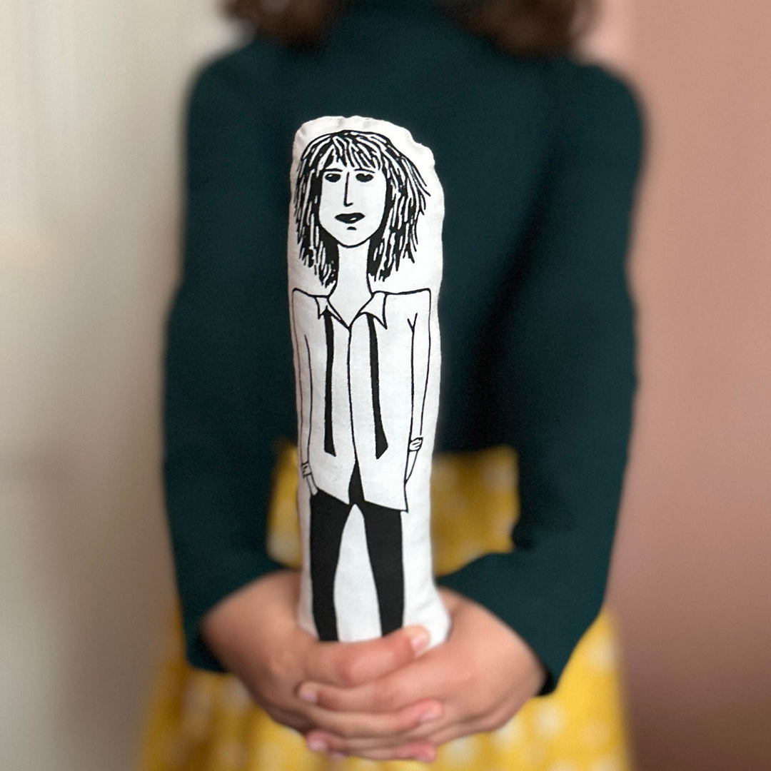 A handmade cushion doll featuring a screen printed black and white design of Patti Smith, held by a child against a blurred background.