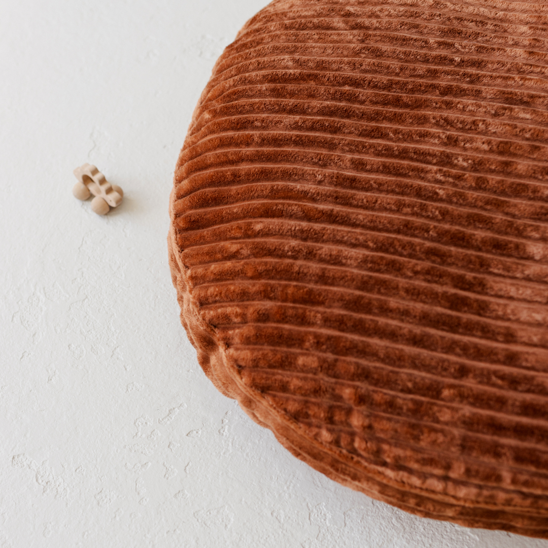 Close up of brown corduroy round floor cushion, showing the chunky soft stripes of the fabric