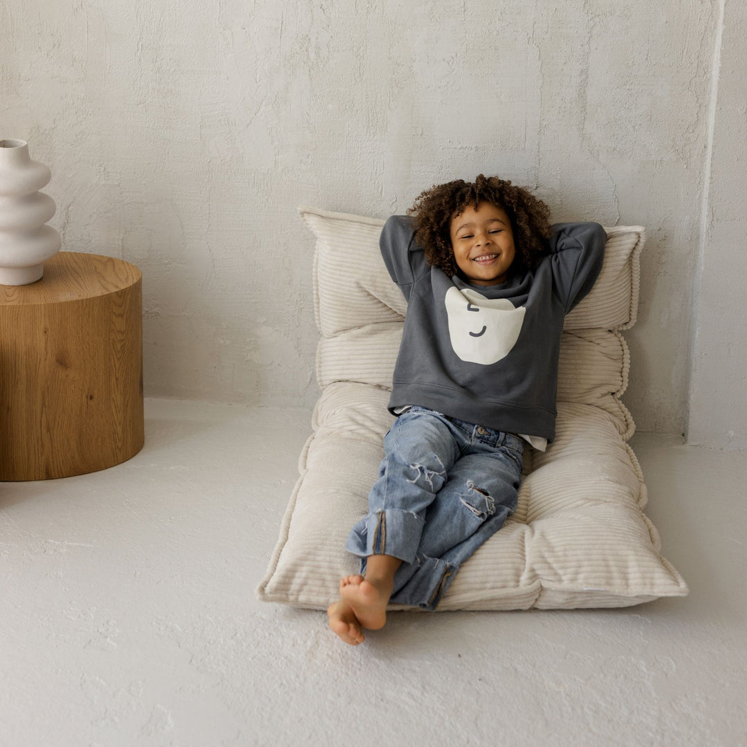 Child sitting on a large cushion with a neutral background