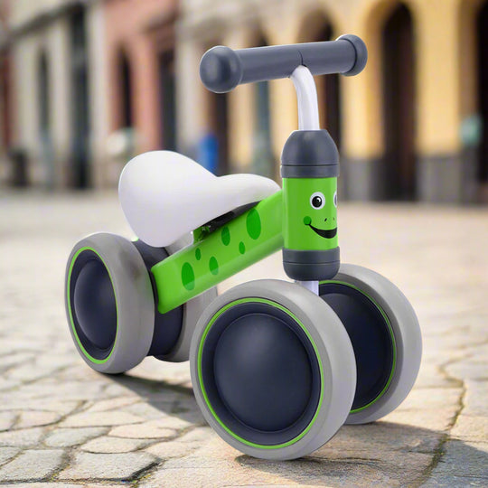 Children's balance bike with green frame and grey wheels on a cobbled pavement background