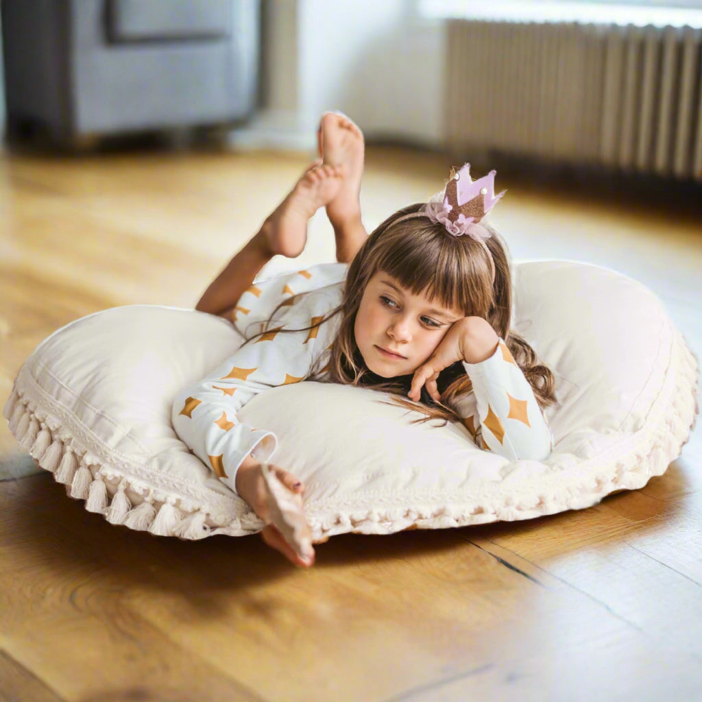 Child lying on a large round pillow with tassels, wearing a princess dress-up outfit.