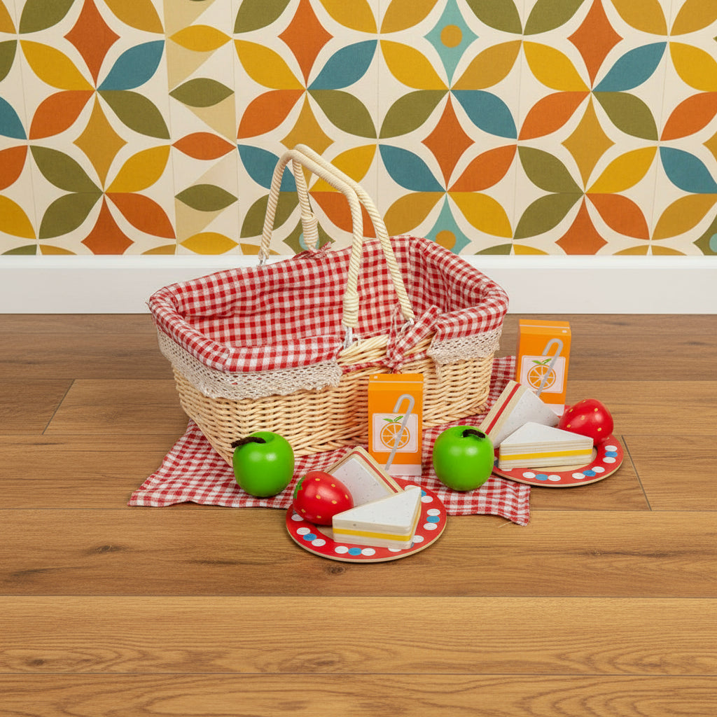 A toy picnic basket set with wooden play food including sandwiches, fruits, and cartons of orange juice, accompanied by plates and a picnic blanket, all laid out on a white background.
