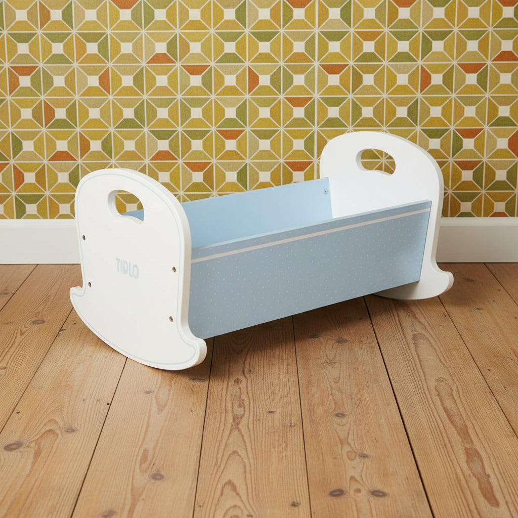 A wooden doll cradle with a light blue base and white accents, featuring a rocking base and a light blue polka dot design.