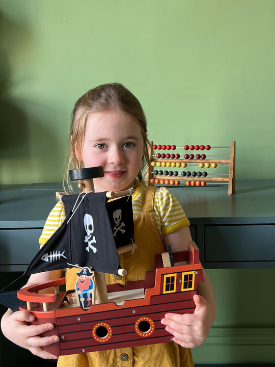 Child holding a toy pirate ship with a green wall and abacus in the background