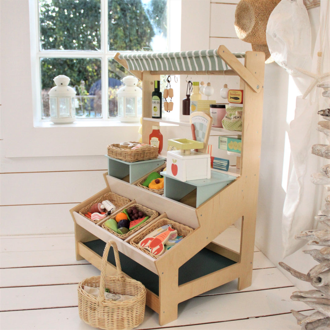 Wooden toy kitchen set with shelves and baskets on a wooden floor.