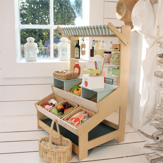 Wooden toy kitchen set with shelves and baskets on a wooden floor.