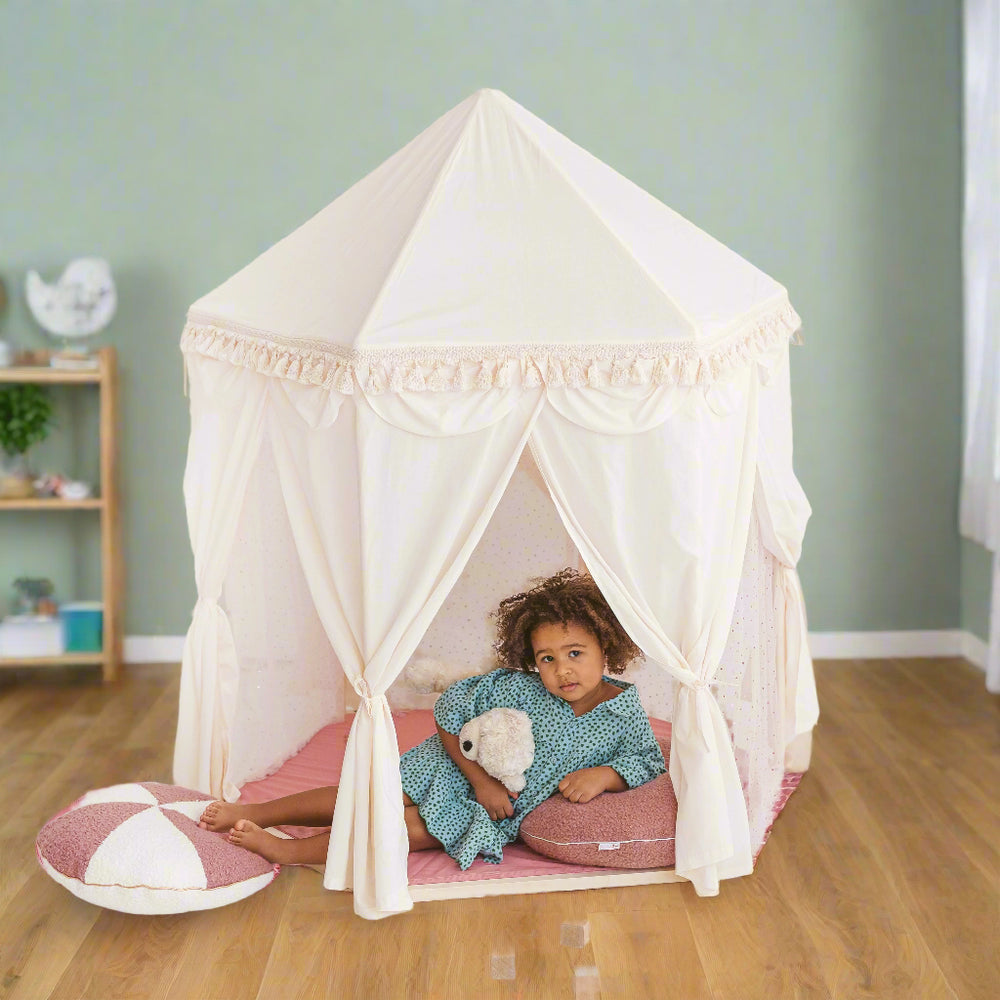 Child lying on their side while holding a teddy bear inside a white pavilion play tent