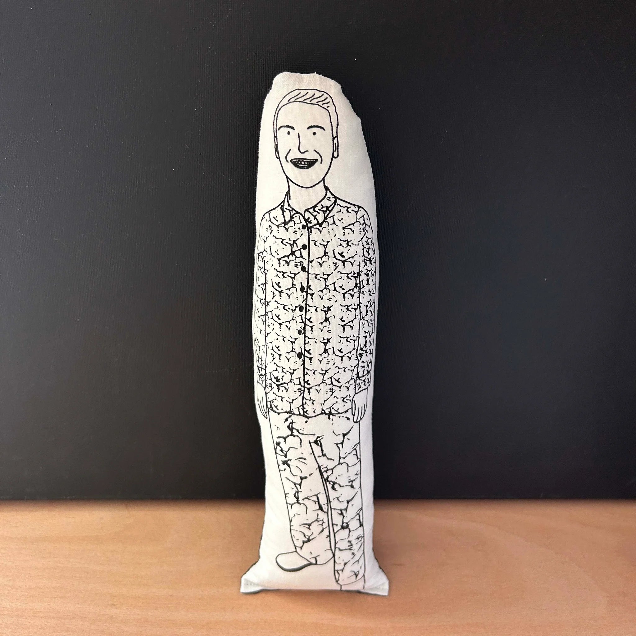 Screen printed doll cushion with white fabric and black illustration depicting comedian and TV resenter Joe Lycett wearing a floral patterned shirt and trousers
