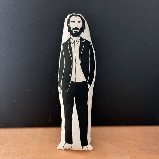 Screen printed doll cushion with white fabric and black illustration depicting actor Keanu Reeves wearing a casual black suit with one hand in his pocket
