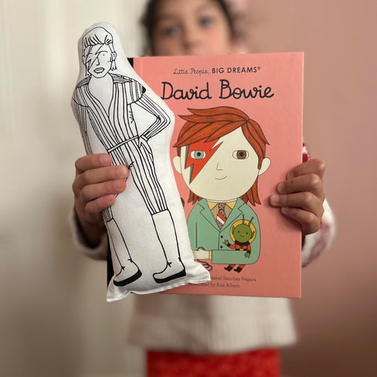 A child holding a cushion doll with a screen printed design of David Bowie, alongside a book cover with David Bowie's illustration.