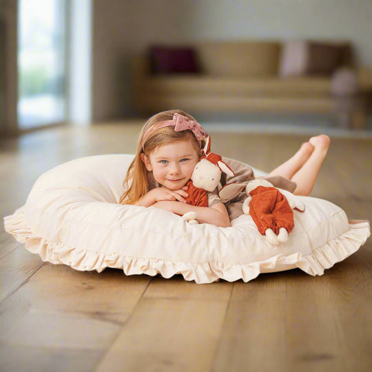 Child lying on a cream coloured large round pillow with ruffled edges