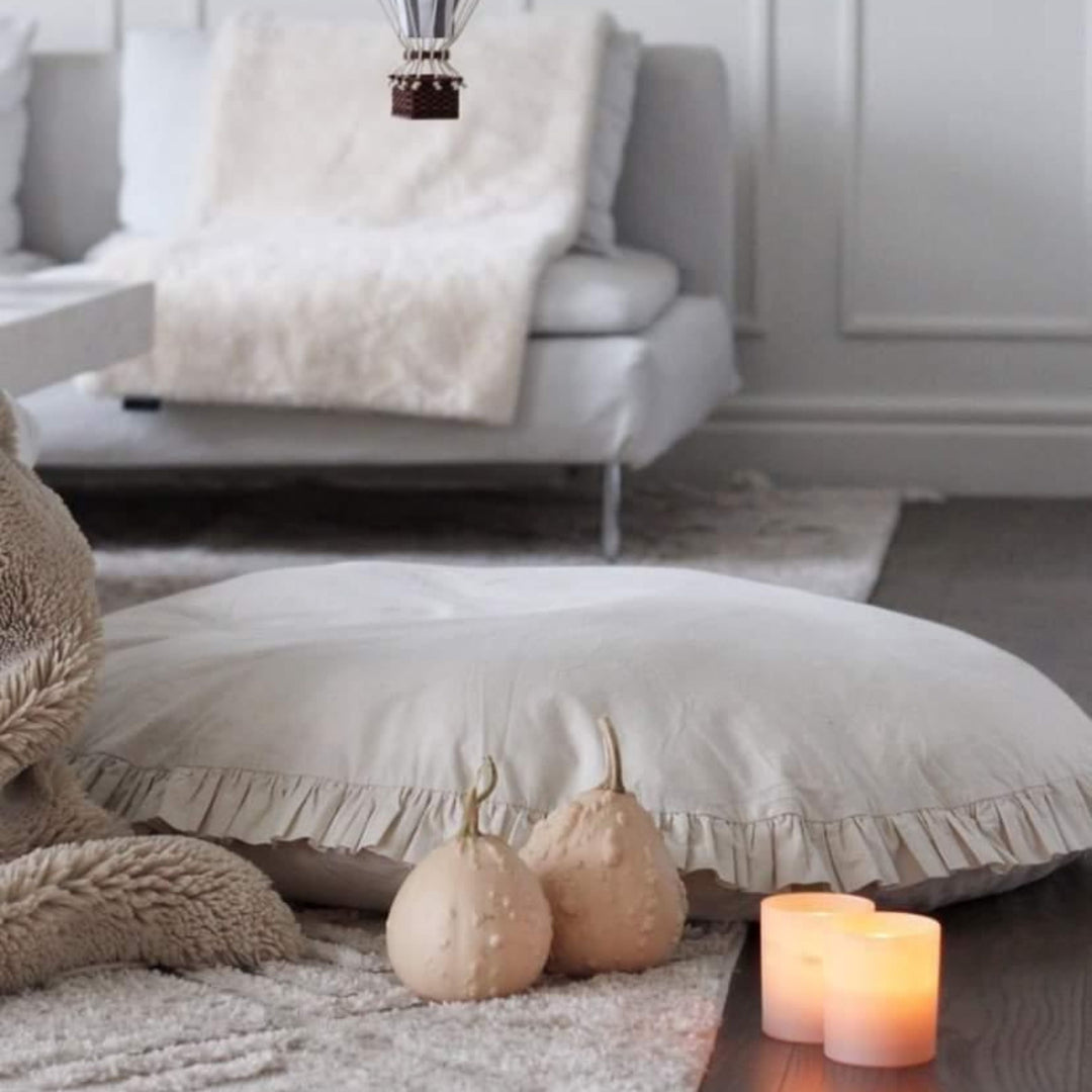 Round pillow on a floor with pumpkins and candles in a cosy living room setting.