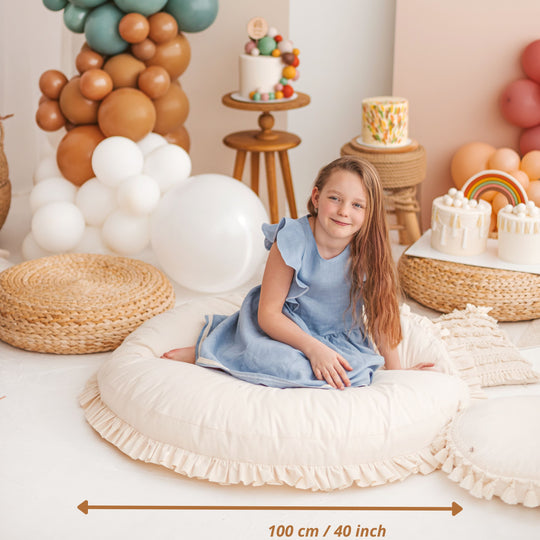 Young girl in a blue dress sitting on a large white cushion with balloons and a cake in the background, with the diameter of the cushion stated: 100cm/40 inches