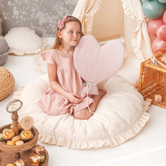 Young girl in a pink dress sitting on a large round cream coloured floor cushion in a child's bedroom