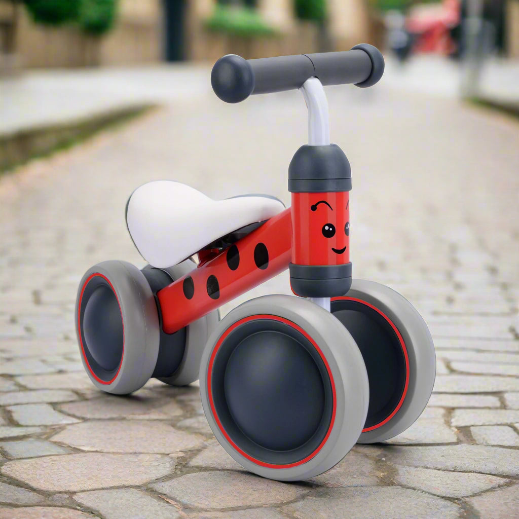 Red balance bike with black spots on main bar, with grey wheels and handlebar with a smiley face on the fron vertical bar