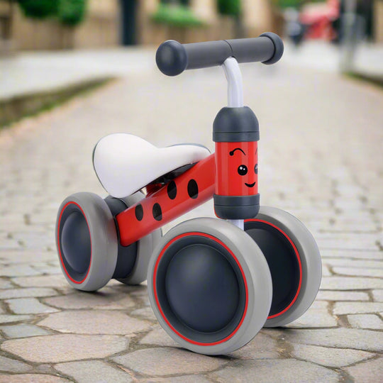 Red balance bike with black spots on main bar, with grey wheels and handlebar with a smiley face on the fron vertical bar