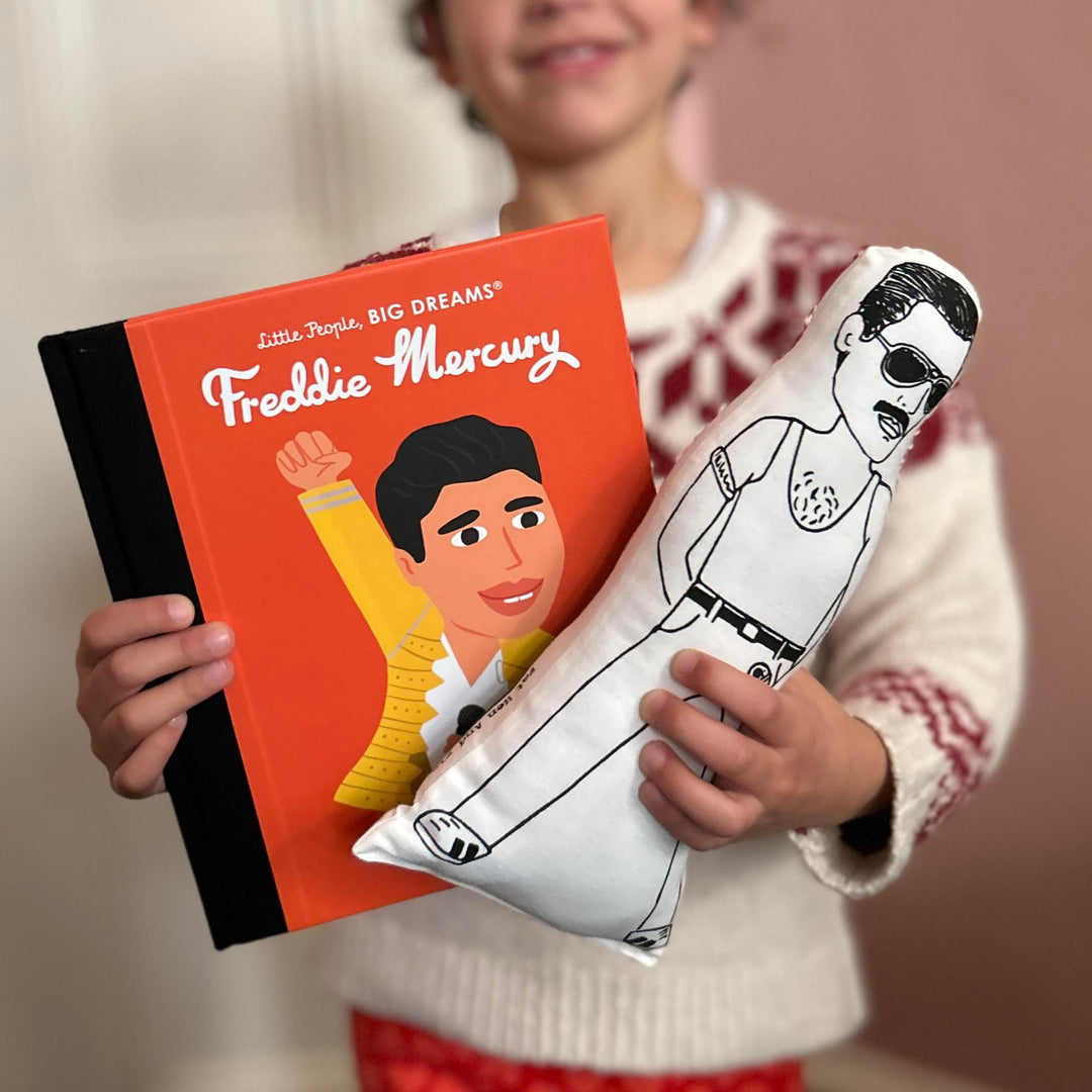 A child holding a screen printed fabric cushion doll depicting Freddie Mercury and a book with Freddie Mercury's illustration on the cover.