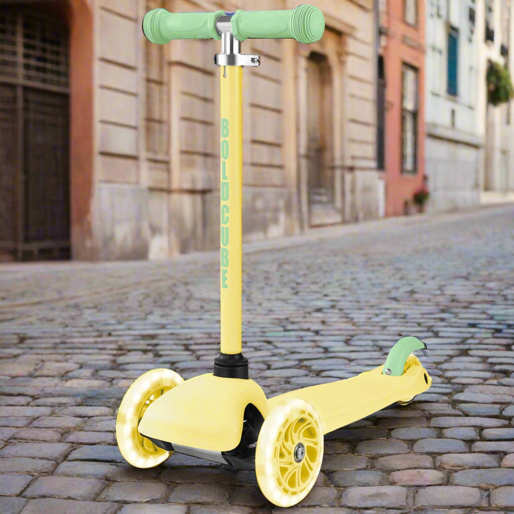 Yellow scooter with yellow wheels, green handlebar and break on a cobbled street with buildings in the background