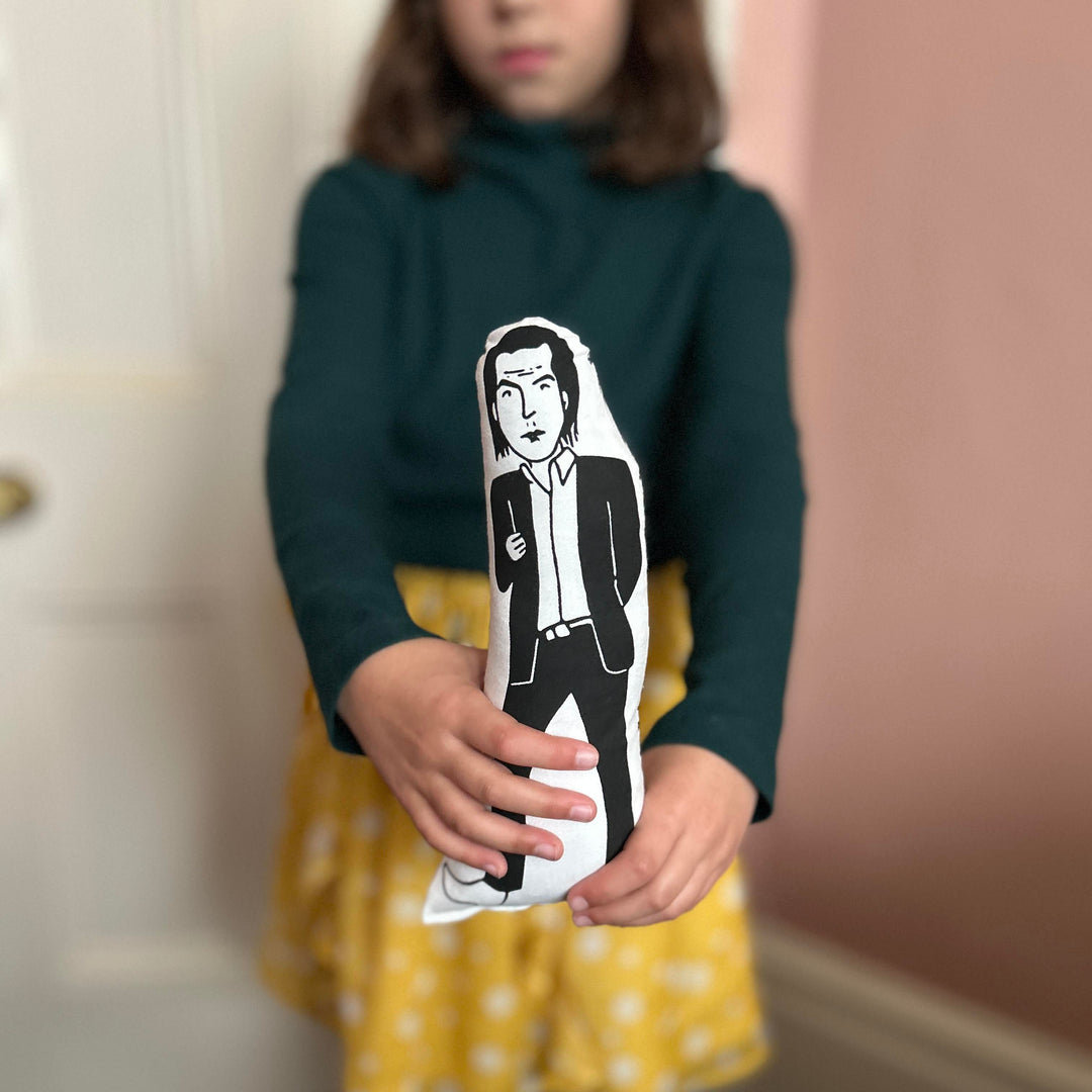 A child holding out a black and white screen printed cushion doll depicting Nick Cave