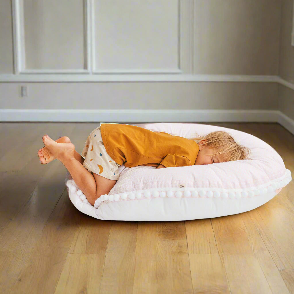 Child lying face down on pale pink floor cushion