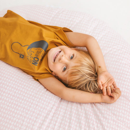 Close up of a child smiling lying on a large pale pink floor cushion