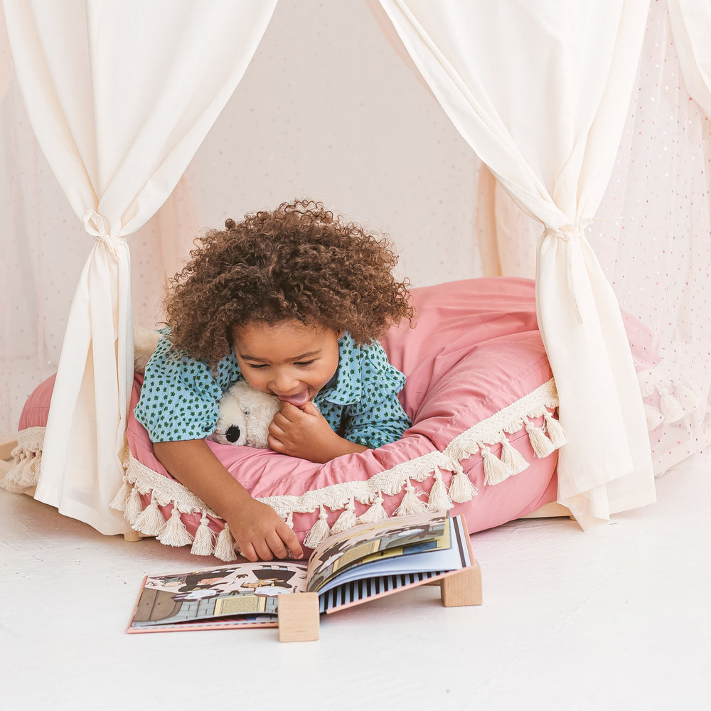 Child reading a book in a pink cushioned play tent with a white curtain