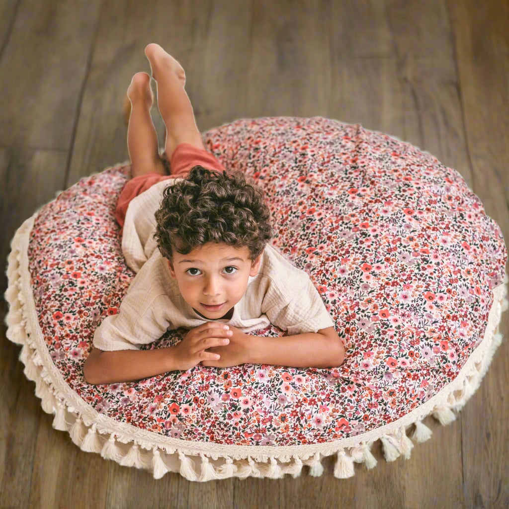 Child lying on a floral-patterned cushion with tassels