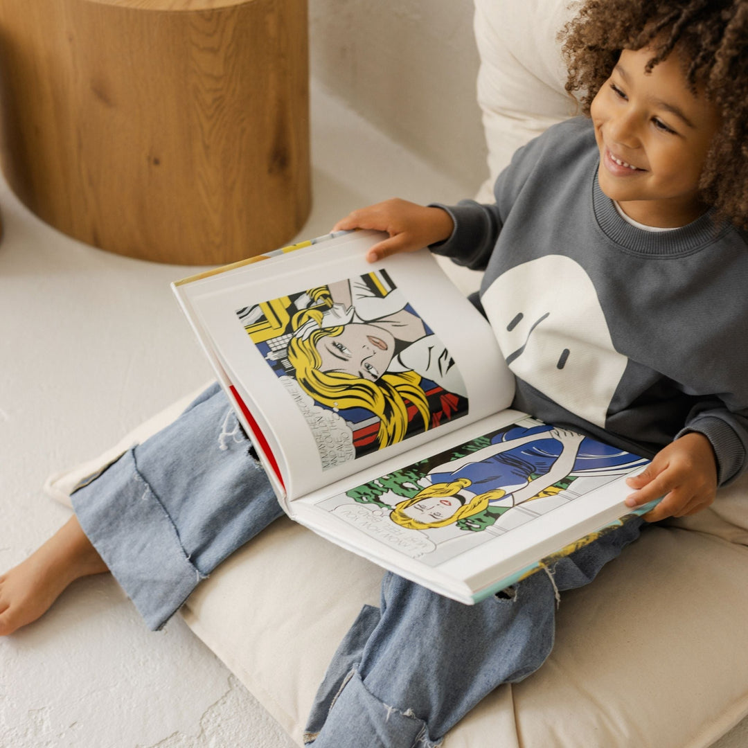 Child sitting on a floor cushion reading a colourful book