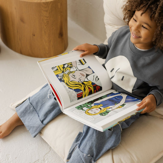 Child sitting on a floor cushion reading a colourful book