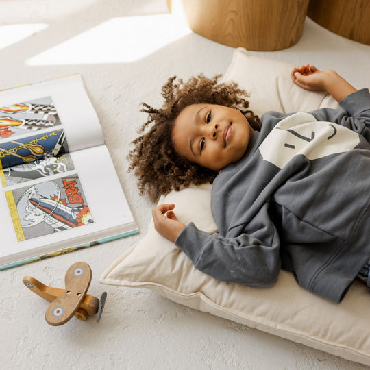 Child lying on a pillow with books and a wooden toy nearby