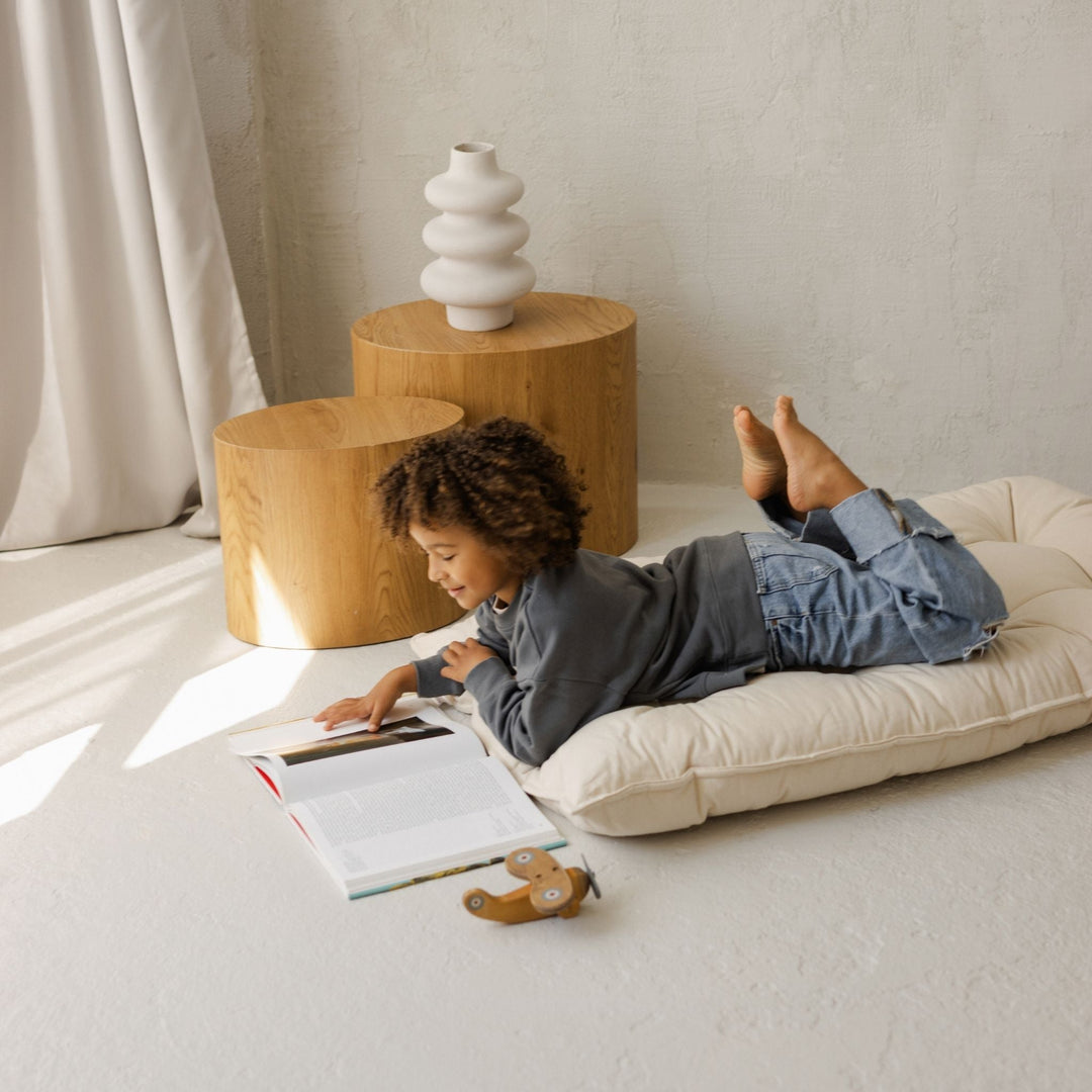 Child lying on a floor cushion reading a book