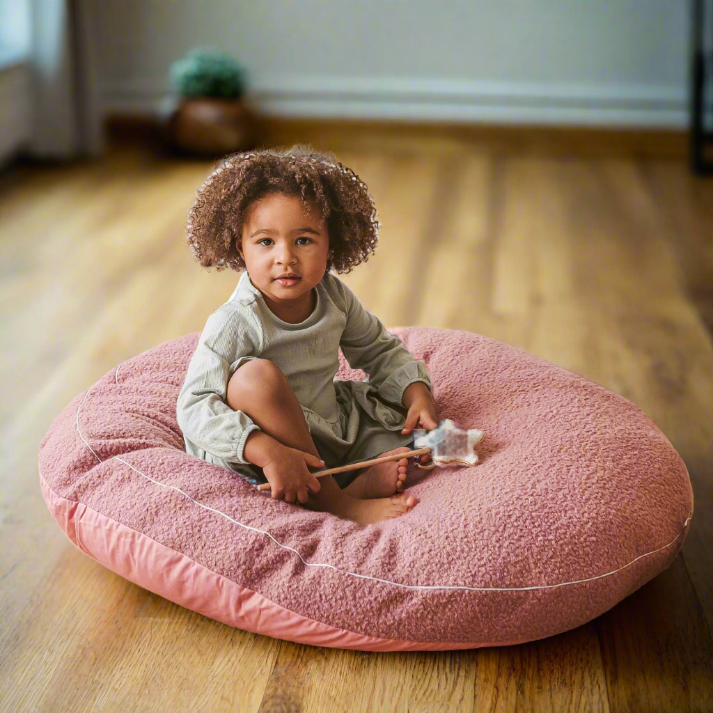 Child sitting on a pink large round floor cushion holding a toy