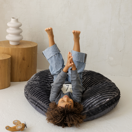Child lying on a round grey cushion with a neutral background
