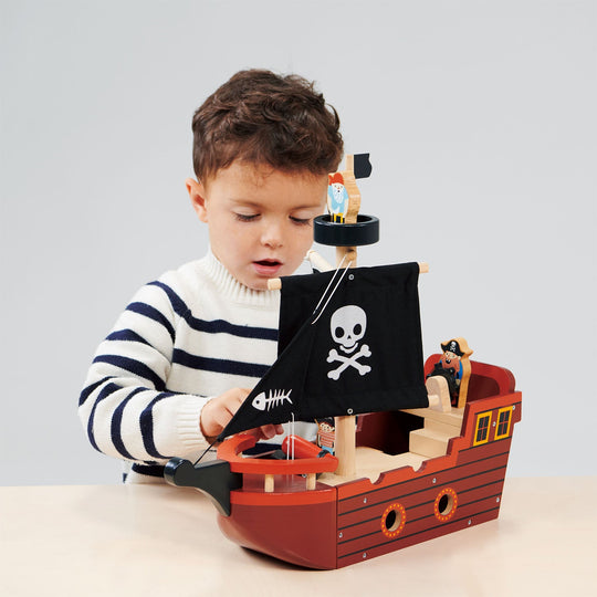 Child playing with a toy pirate ship on a light grey background