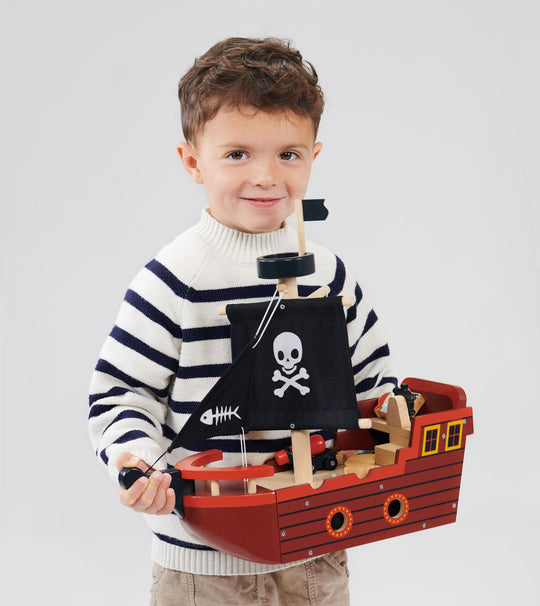 Child wearing a striped sweater holding a toy pirate ship against a plain background