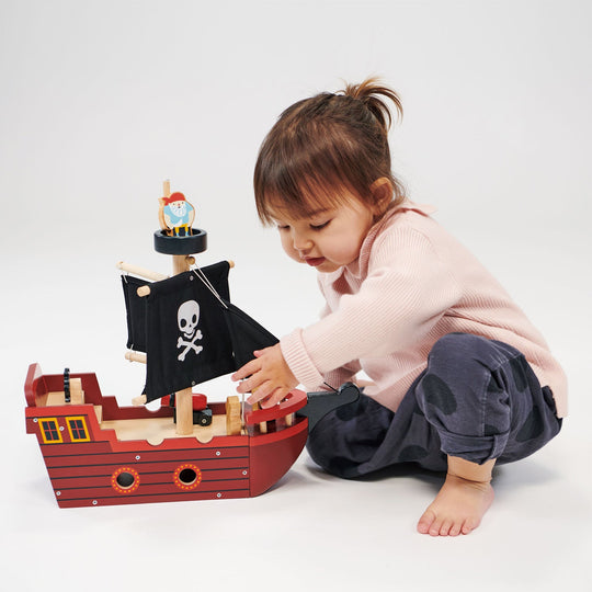 Child playing with a toy pirate ship on a white background