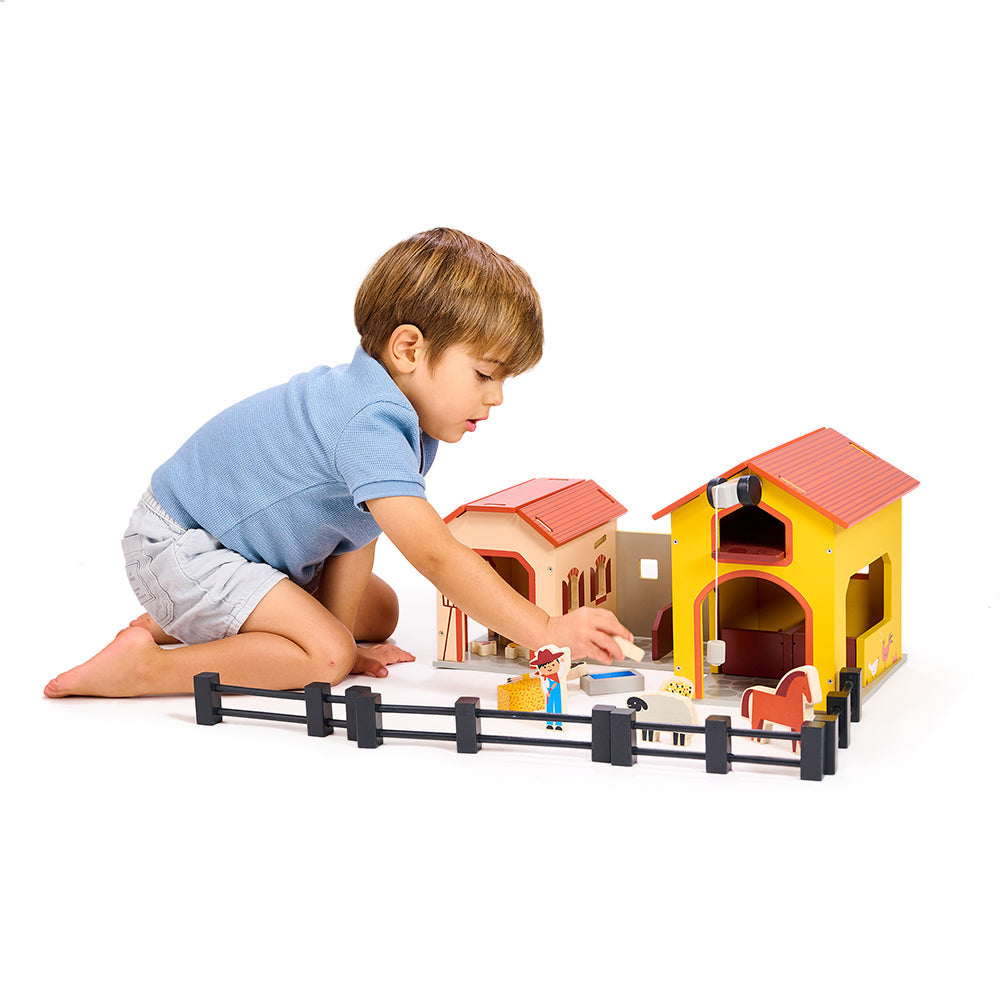 Child playing with a toy barn set on a white background
