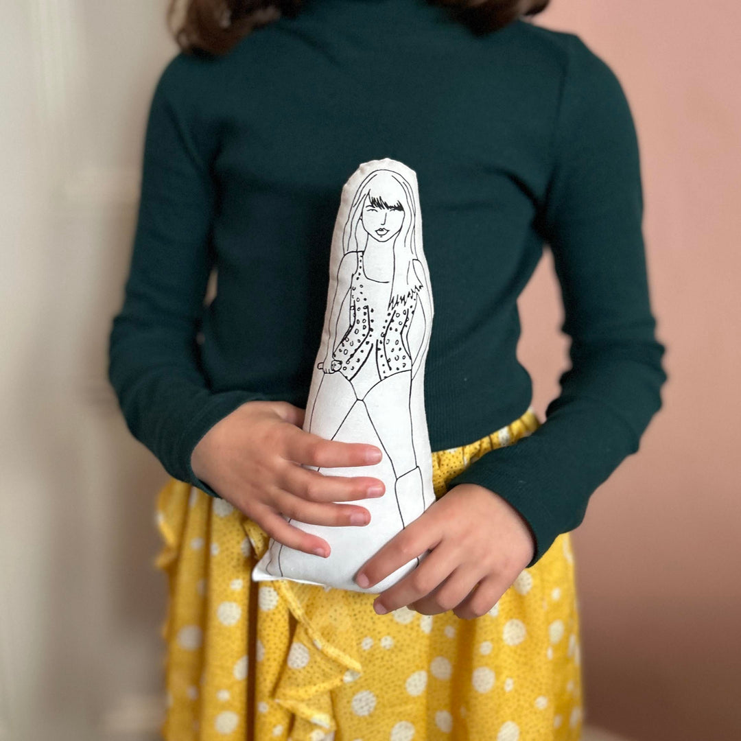 A child holding a black and white screen printed cushion doll depicting a stylised image of Taylor Swift.