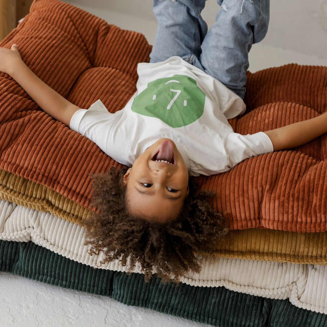 Child lying on a stack of colourful cushions with a white shirt and blue jeans.