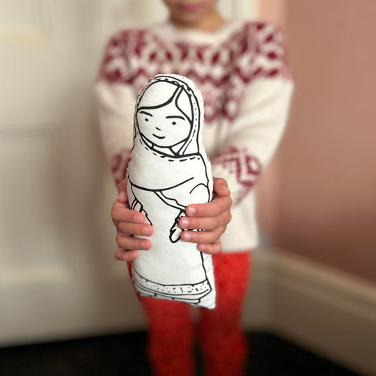 A child holding out a screen printed doll cushion of Malala Yousafai