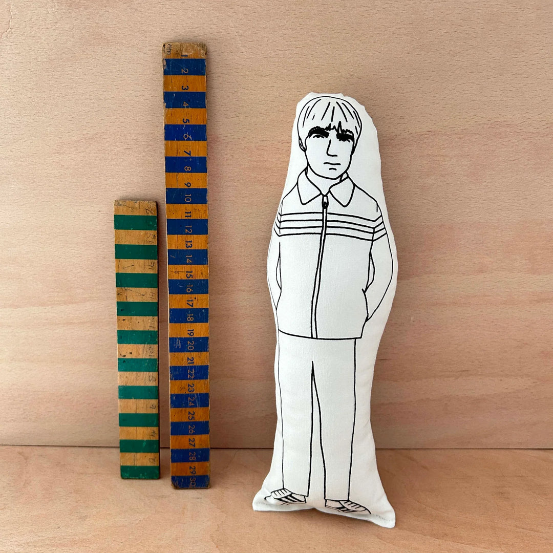 Screen printed doll cushion of Noel Gallagher next to two wooden rulers against a wooden background