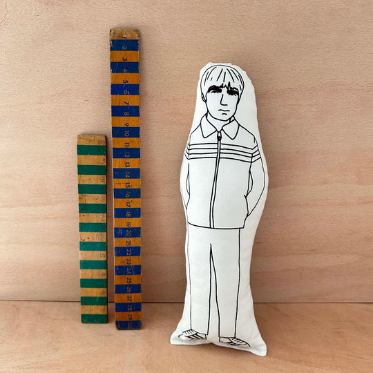 Screen printed doll cushion of Noel Gallagher next to two wooden rulers against a wooden background