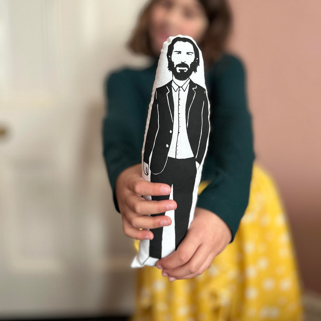 A child holding out a screen-printed cushion doll featuring a black and white image of Keanu Reeves.
