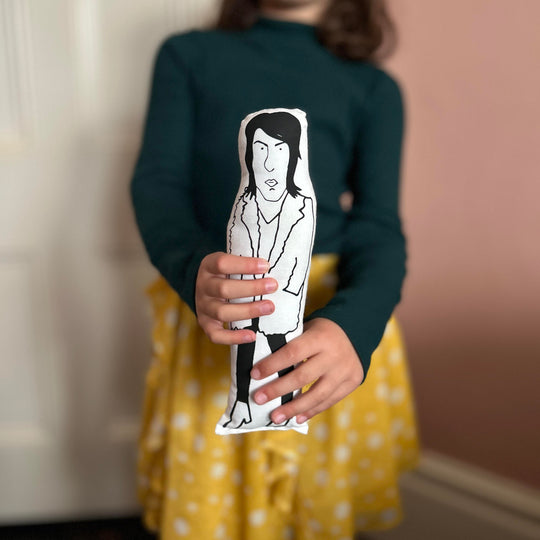 A child holding out a black and white screen printed doll cushion of Noel Fielding