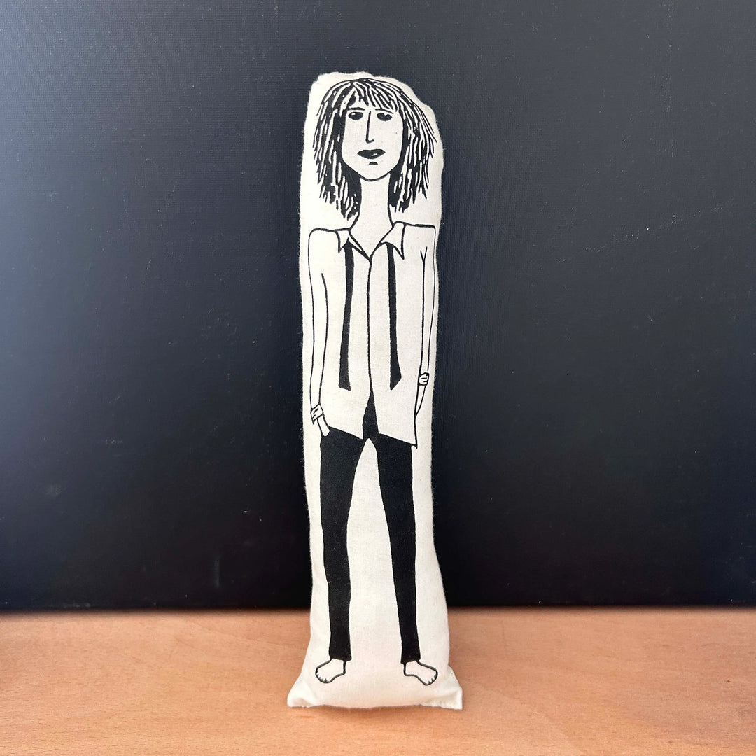 Screen printed doll cushion with white fabric and black illustration depicting rock musician Patti Smith wearing black skinny trousers, barefoot and with a white shirt and undone black tie, with shaggy hair