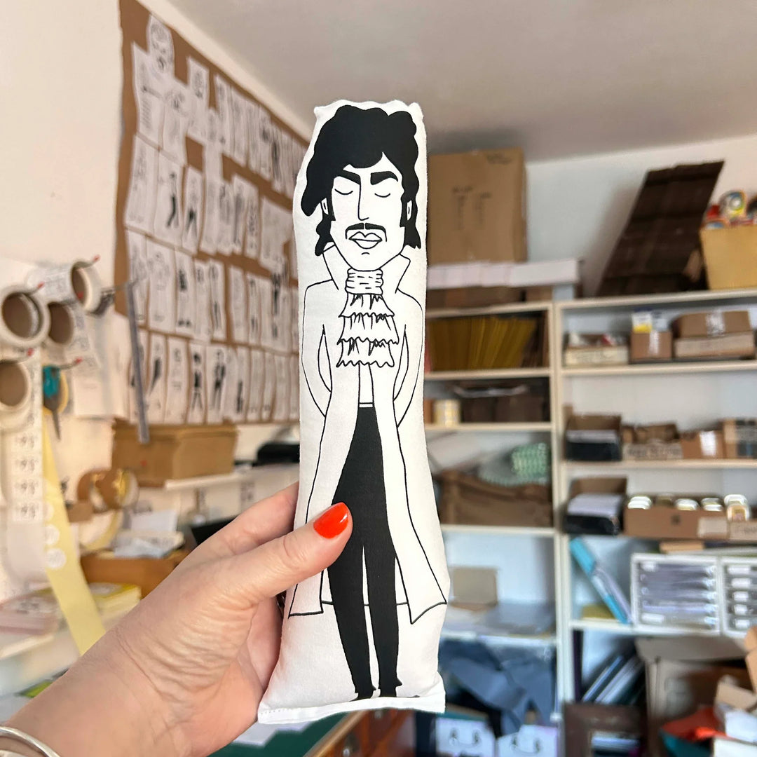 Hand holding screen printed cushion doll of Prince against an out of focus interior setting