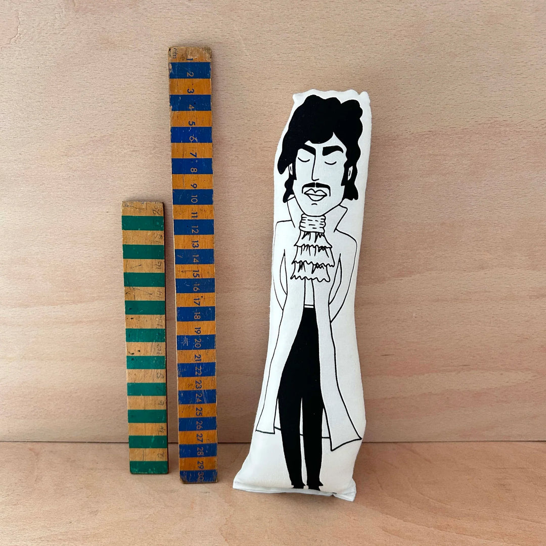 Screen printed cushion doll of Prince next to two wooden rulers against a wooden background